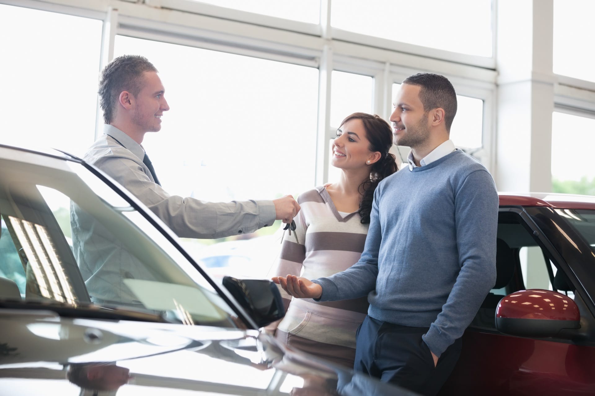 A salesman handing car keys to a smiling couple at a dealership